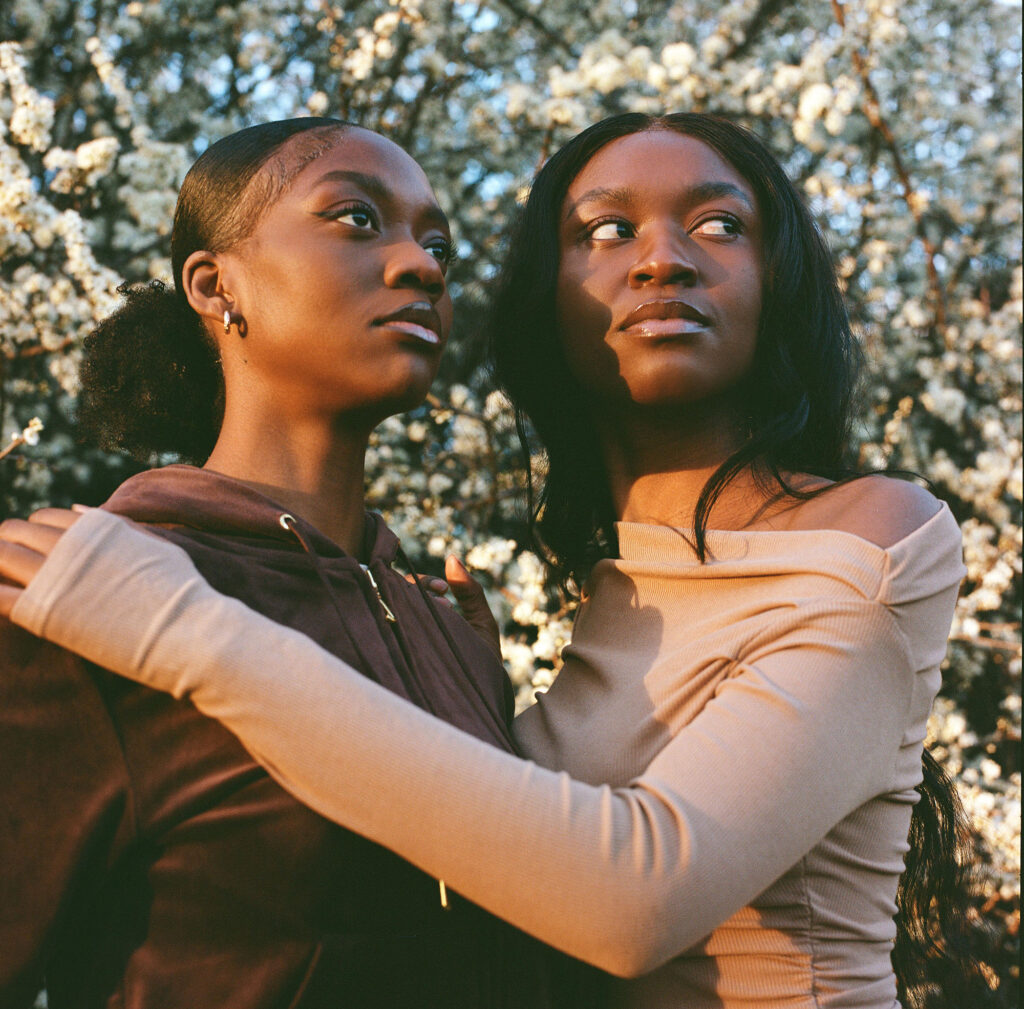 Two women standing side by side, reflecting strength and unity against a backdrop of blossoms.