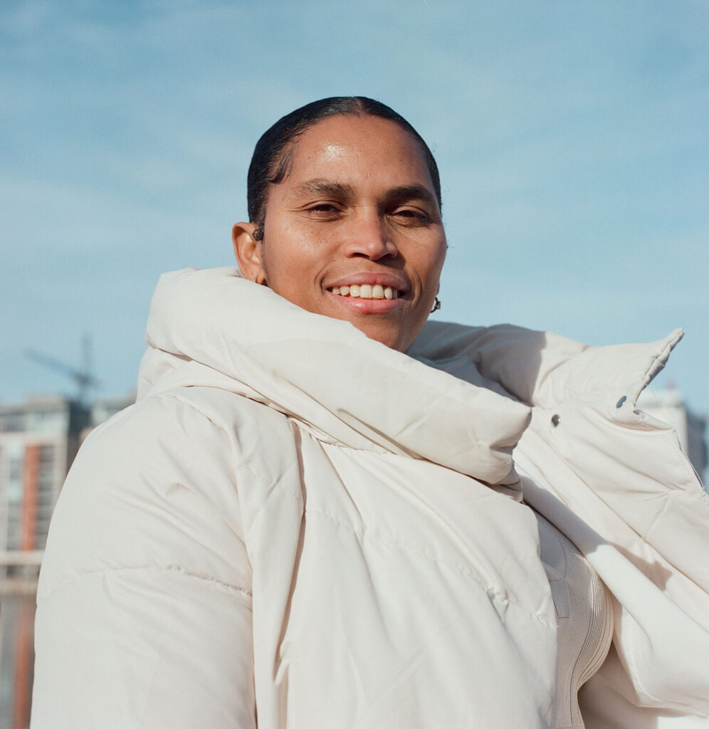 Portrait of a smiling person wearing a white winter coat, with an urban background and a clear sky