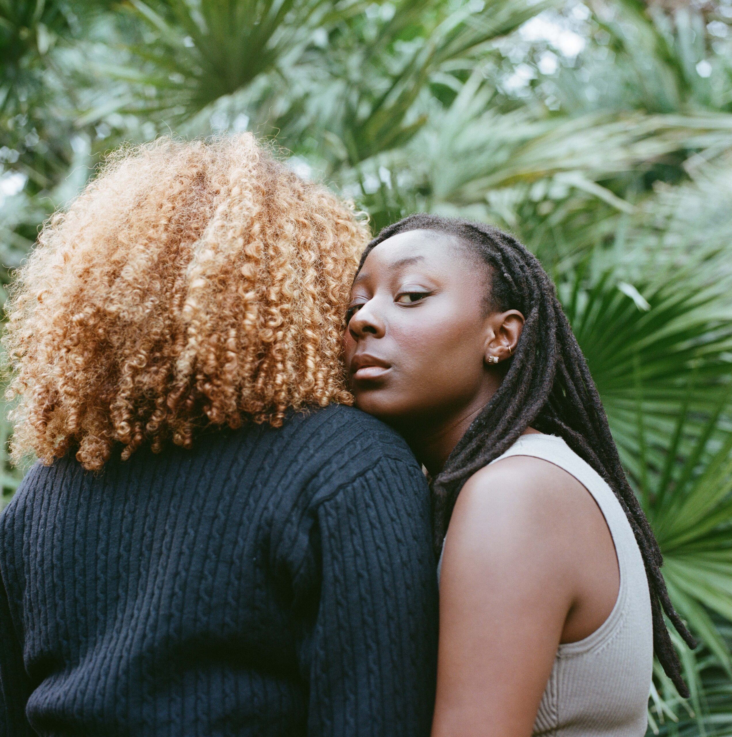 Two women sharing an intimate moment, illustrating friendship and support in a green environment.