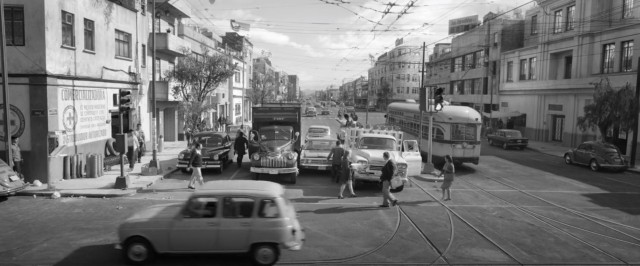 A busy city street filled with vehicles and pedestrians crossing. The atmosphere is chaotic, with a mix of cars and buses in motion.