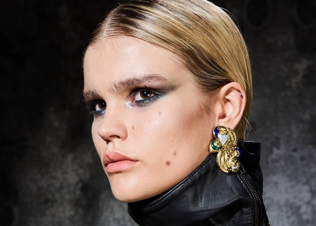 Portrait of model wearing gold and green statement jewelry and black voluminous dress from Jayne Pierson’s SS25 “Annwn” collection, inspired by Welsh mythology.