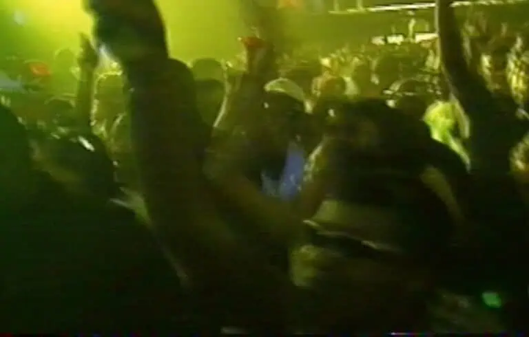 Low-light VHS capture of rave crowd dancing at night under green lighting