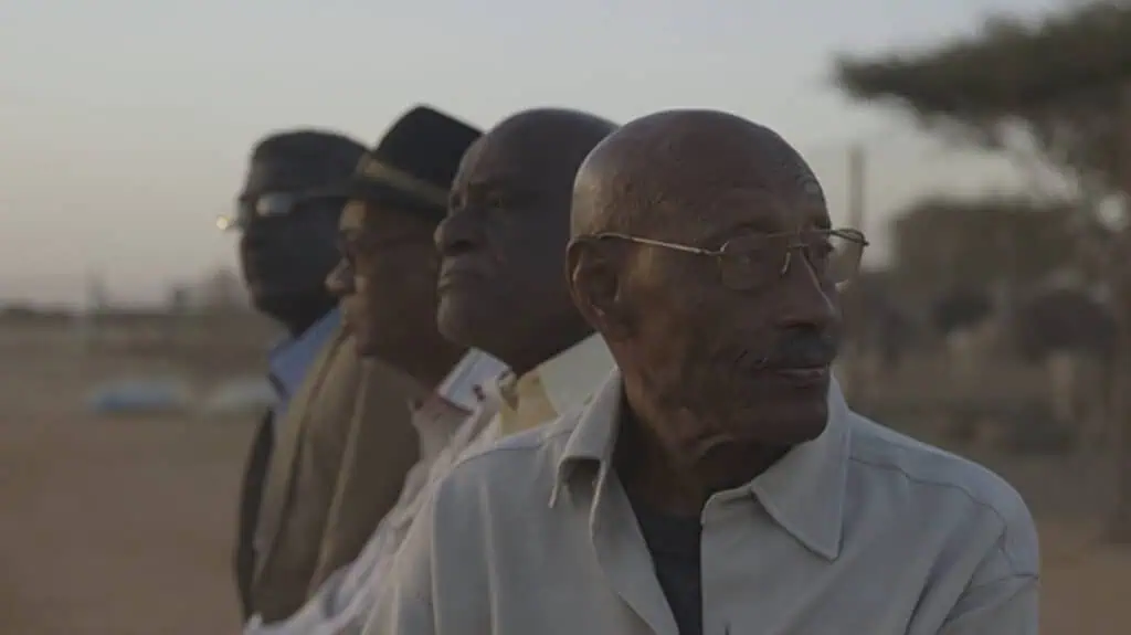 Still from Talking About Trees (2019) showing four elderly men looking into the distance at dusk, symbolising resilience and collective memory in Sudanese cinema.