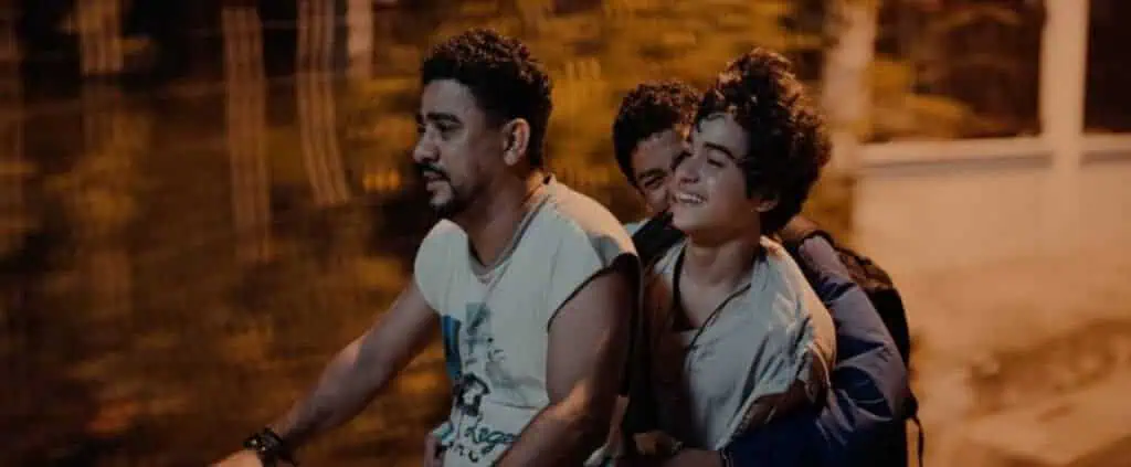 Still from a film by José María Cabral (2024) showing two men and a boy riding a motorbike at night, capturing intimacy and generational connection.
