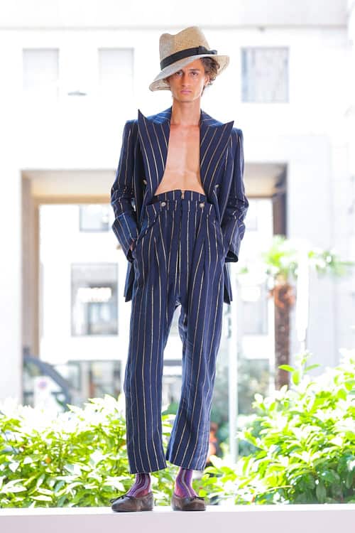 Model wearing navy pinstripe suit with deep neckline and straw hat from Vivienne Westwood Men’s collection at Milan Fashion Week.