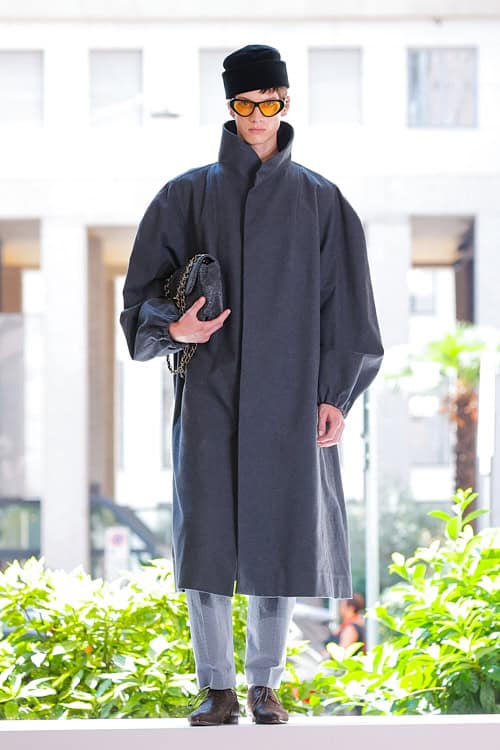 Model wearing oversized gray coat, tailored trousers, and amber sunglasses from Vivienne Westwood Men’s collection at Milan Fashion Week.