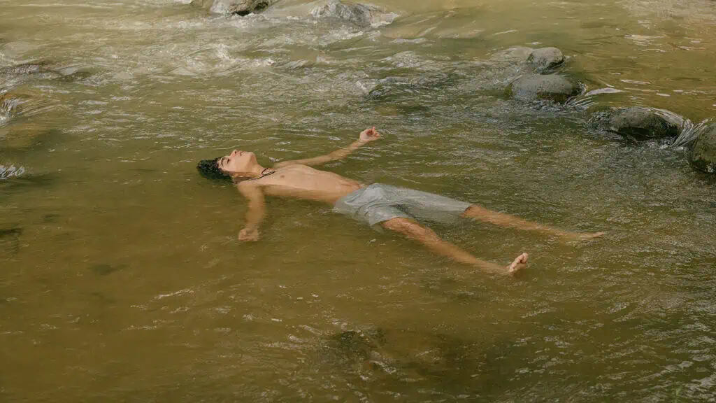 Pablo floating alone in mountain river, moment of introspection in Tiguere film