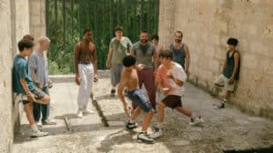 Teen boys boxing in stone courtyard under adult supervision, tigueraje training in Tiguere