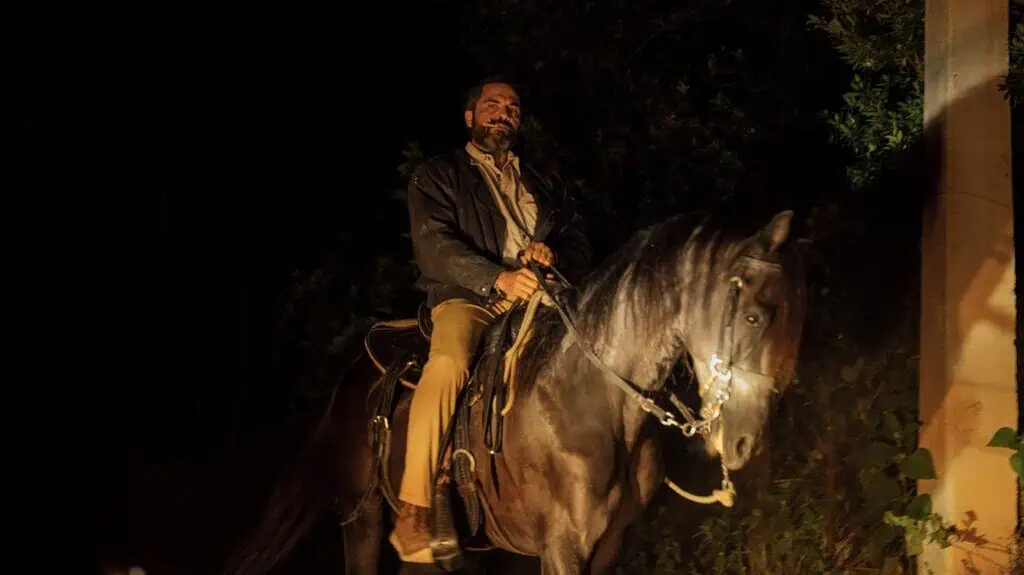 Alberto riding a black horse at night, father figure in Tiguere masculinity bootcamp