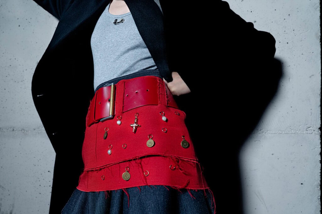 Close-up of a red belt with dangling charms, layered over a denim skirt