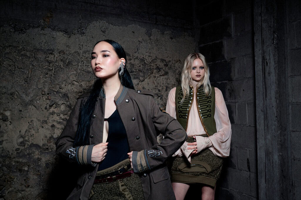 Two models standing in a raw concrete space, wearing military-inspired jackets with vintage tailoring