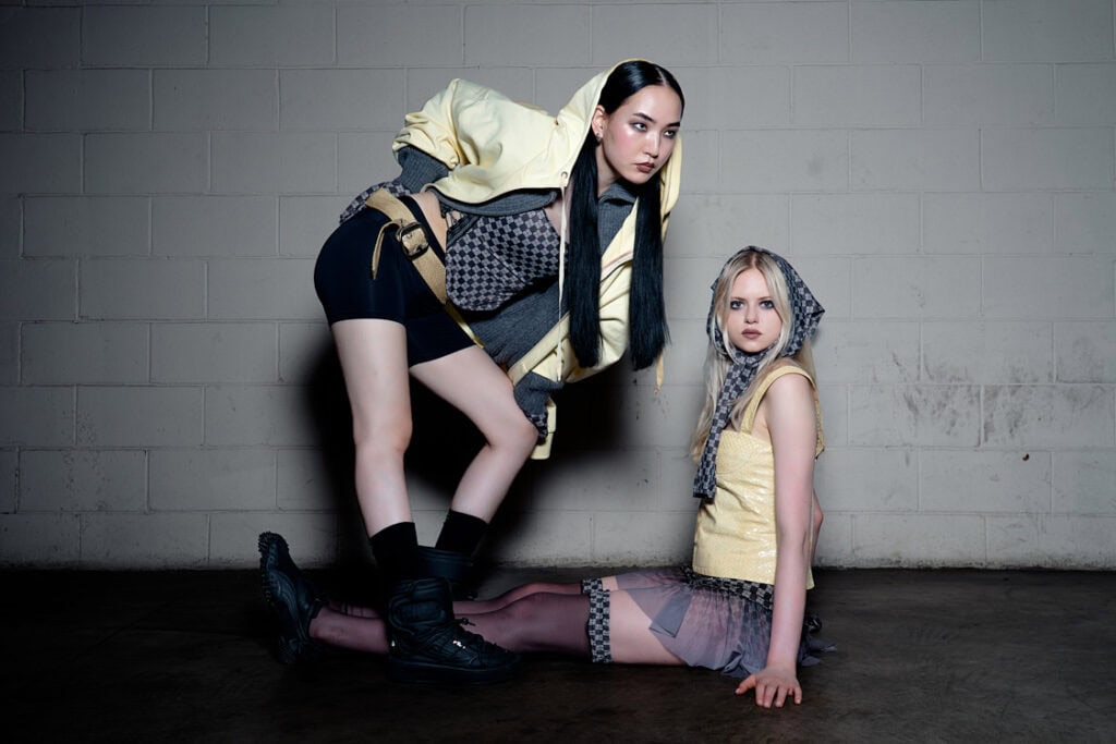 wo models in yellow and gray sporty outfits, posed against a light brick wall