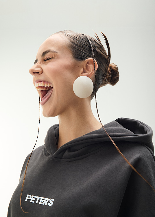 Smiling woman wearing large circular earrings and a black hoodie with 'PETER'S' branding