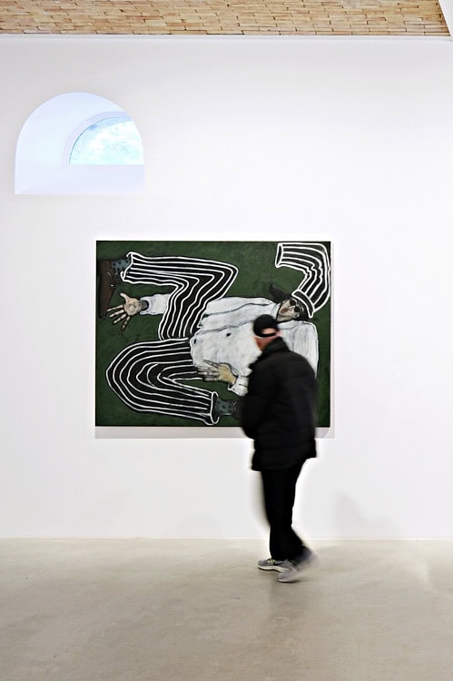 Gallery visitor walking past Jack Penny’s artwork of a twisted chef figure on a green background.