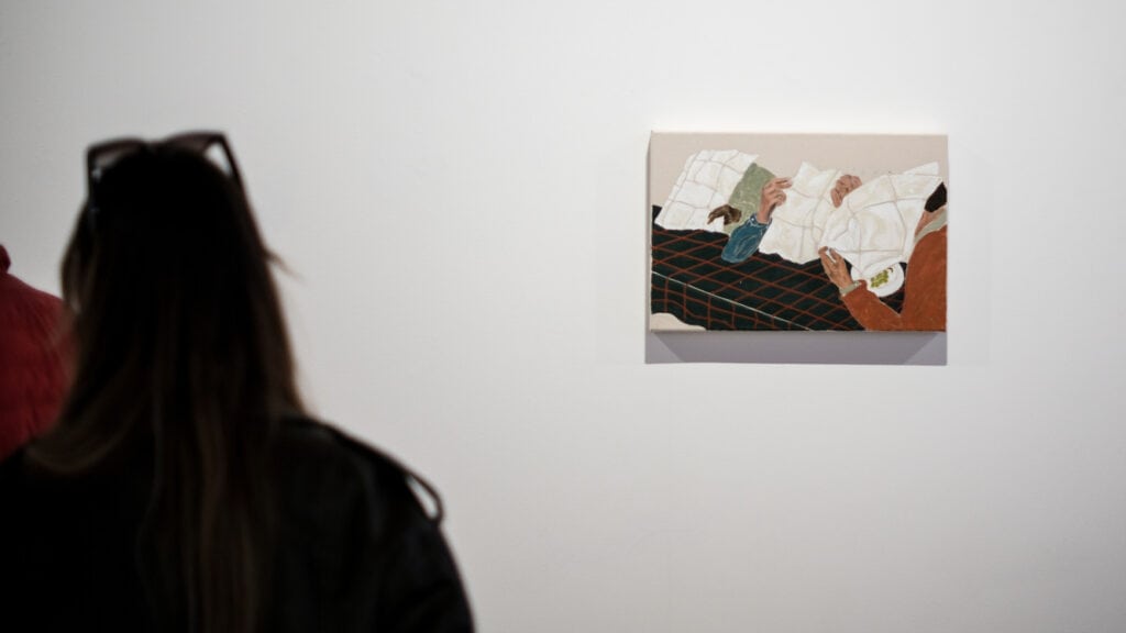 Viewer observing a small Jack Penny painting of masked figures reclining at a table.