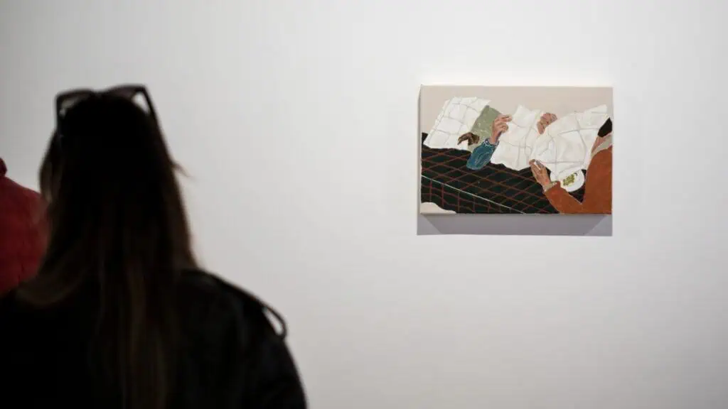 Viewer observing a small Jack Penny painting of masked figures reclining at a table.