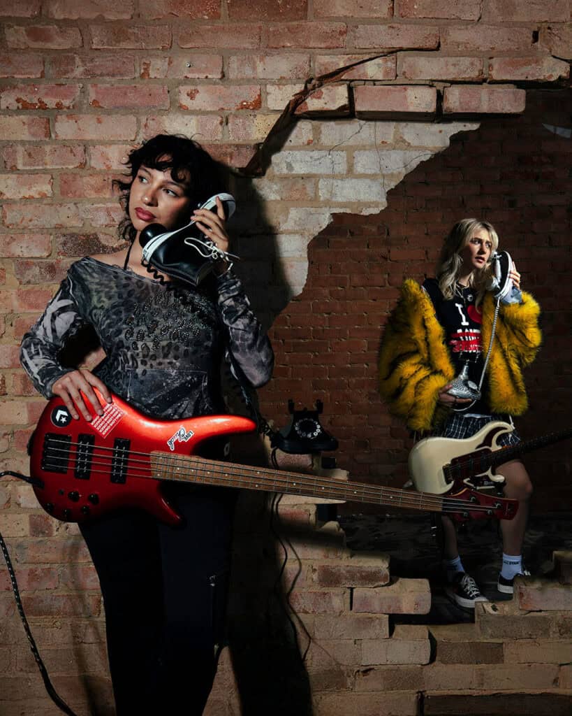 Two musicians posing with electric guitars and Converse sneakers used as phones, during A Voice Amplified in London