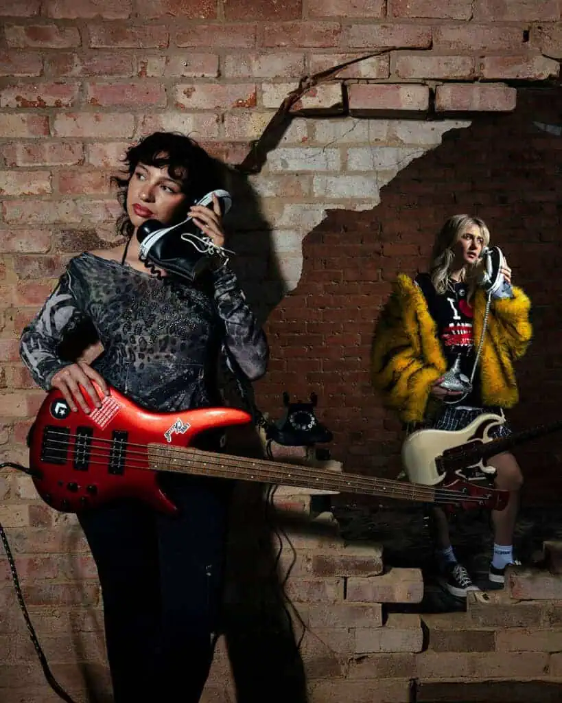 Two musicians posing with electric guitars and Converse sneakers used as phones, during A Voice Amplified in London
