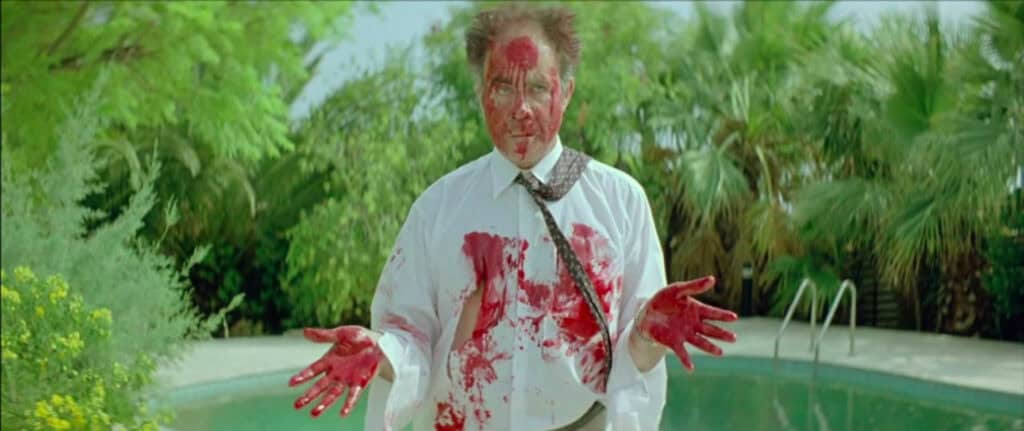 A man in a white shirt drenched in blood stands in front of a pool, hands raised and dazed, highlighting the film’s shocking violence – Dogtooth (2009)