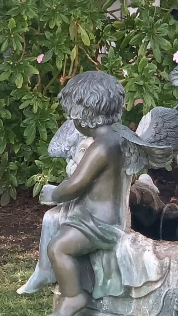 Close-up of a weathered cherub statue in a garden, appearing to drink from a fountain