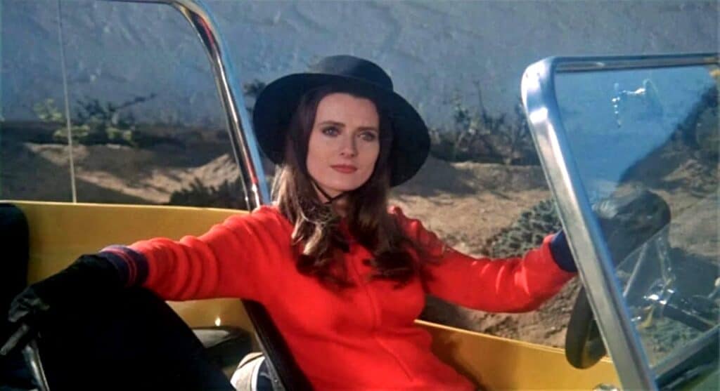 Iconic shot from Stephanie Rothman's 'The Velvet Vampire': a confident woman in a red jacket and black hat sits in a yellow convertible, embodying the film's feminist and countercultural spirit.