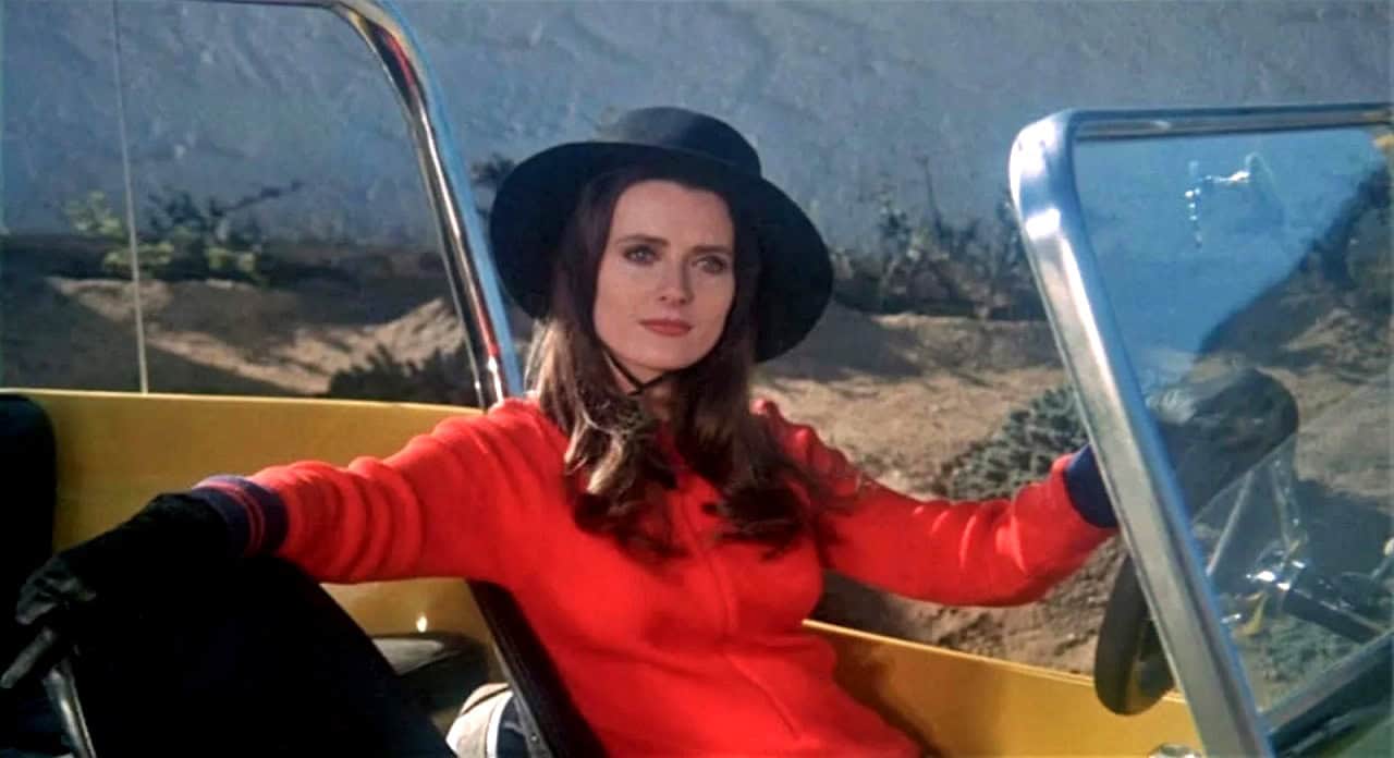 Iconic shot from Stephanie Rothman's 'The Velvet Vampire': a confident woman in a red jacket and black hat sits in a yellow convertible, embodying the film's feminist and countercultural spirit.