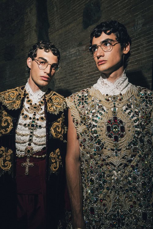 Two models in ornate, gem-encrusted garments with crucifix motifs, photographed backstage – Dolce & Gabbana Alta Sartoria 2025.
