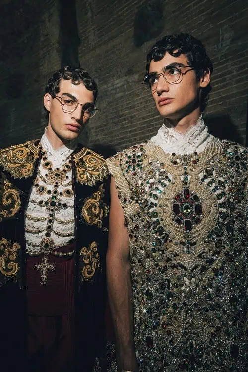Two models in ornate, gem-encrusted garments with crucifix motifs, photographed backstage – Dolce & Gabbana Alta Sartoria 2025.