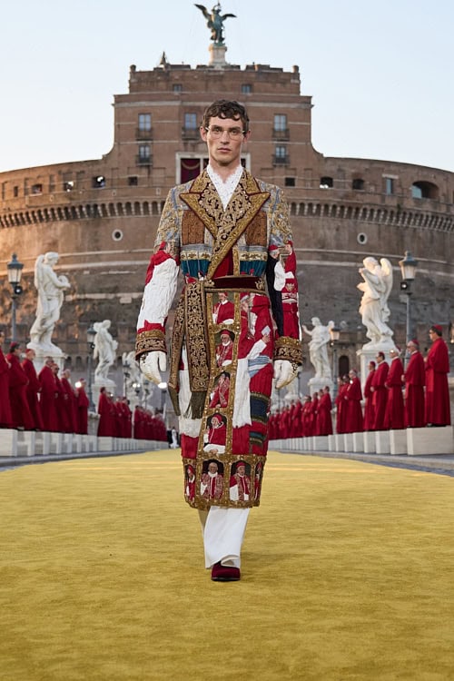 Runway model in a richly embroidered coat featuring religious iconography, walking across Ponte Sant’Angelo – Dolce & Gabbana Alta Sartoria 2025.