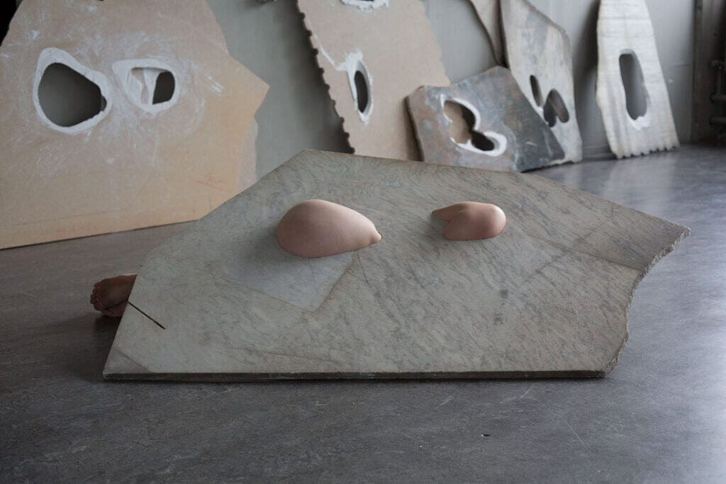 Sculptural marble piece on the floor featuring smooth, flesh-coloured forms emerging from its surface.