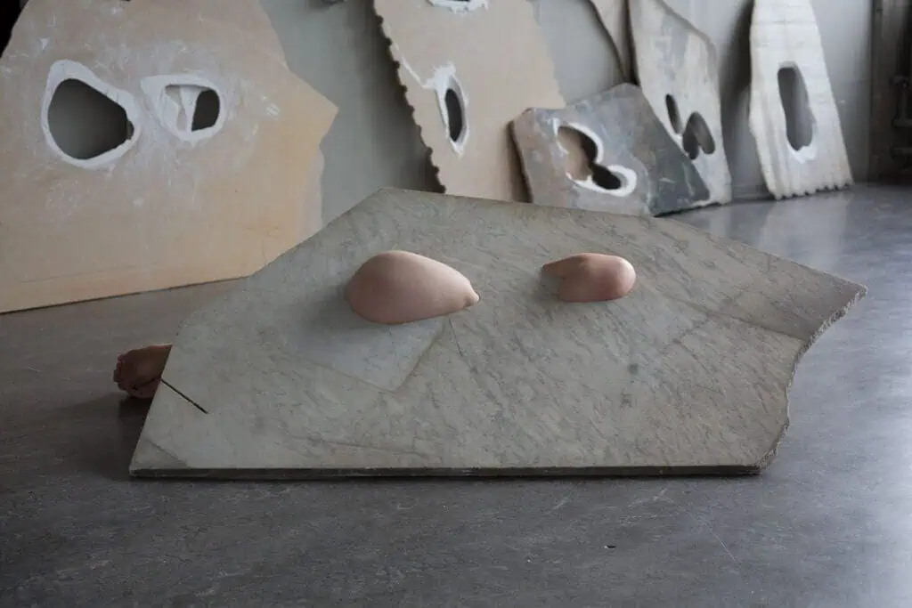 Sculptural marble piece on the floor featuring smooth, flesh-coloured forms emerging from its surface.