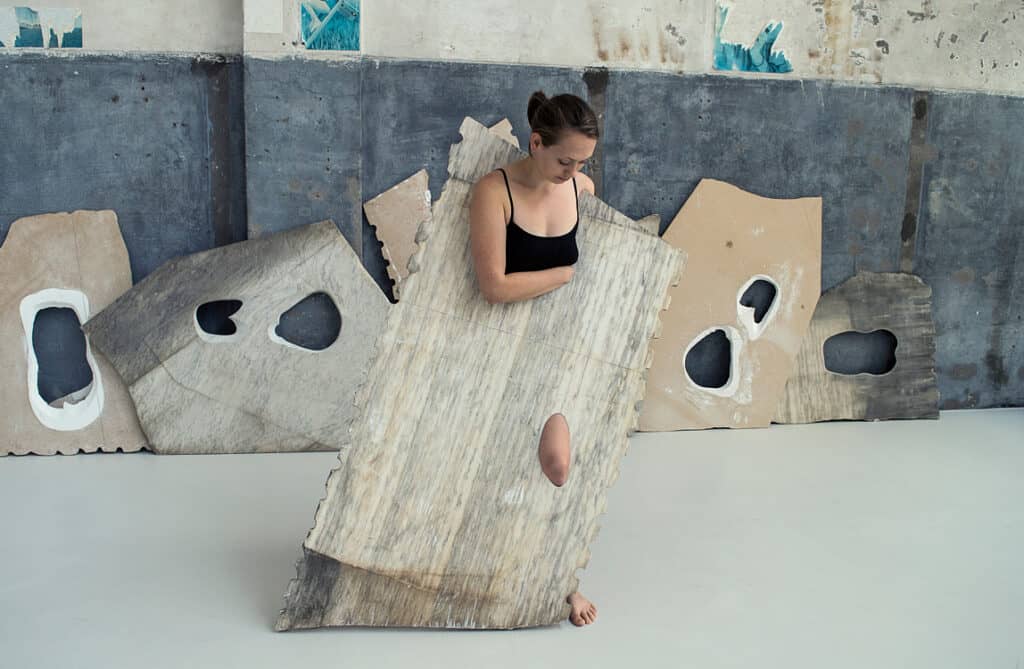 Milena Naef posing inside a large marble slab with cut-out shapes in an industrial studio setting.