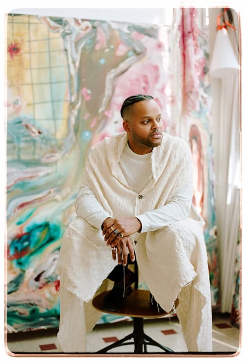 Portrait of artist Manuel Mathieu seated in his studio, surrounded by large colorful abstract canvases.