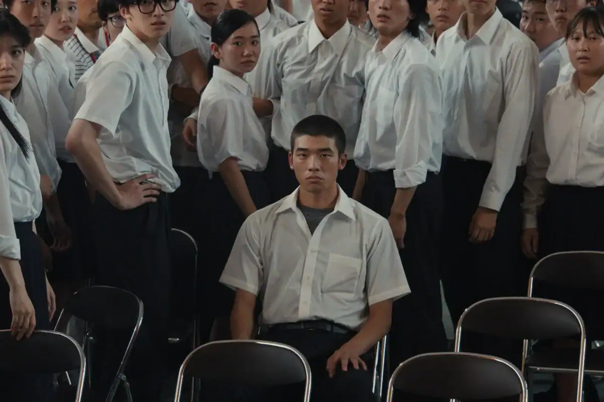 Kou sits isolated among classmates during a tense school assembly in Happyend.