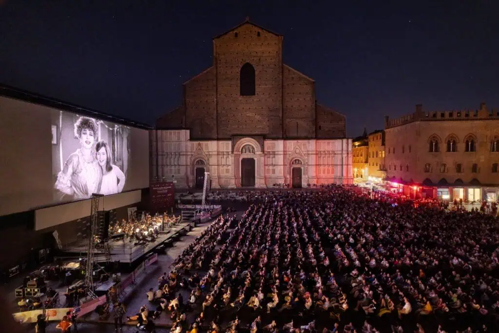 Nighttime outdoor screening at Bologna’s Il Cinema Ritrovato film festival in Piazza Maggiore, with a large audience watching a silent film.