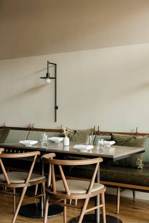 Minimalist dining room with green seating and wooden chairs inside The Silver Birch.