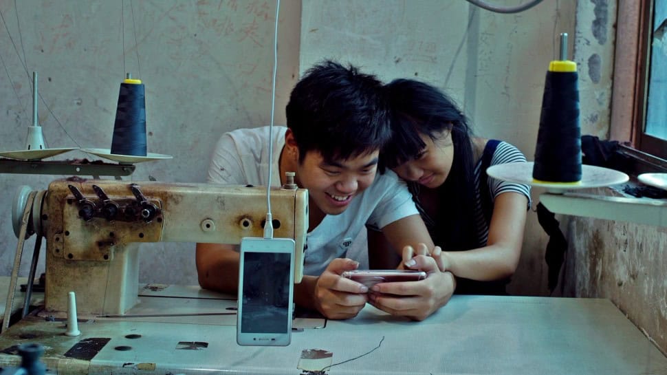 Two young factory workers sharing a phone moment in Zhili, scene from Wang Bing’s Youth trilogy.