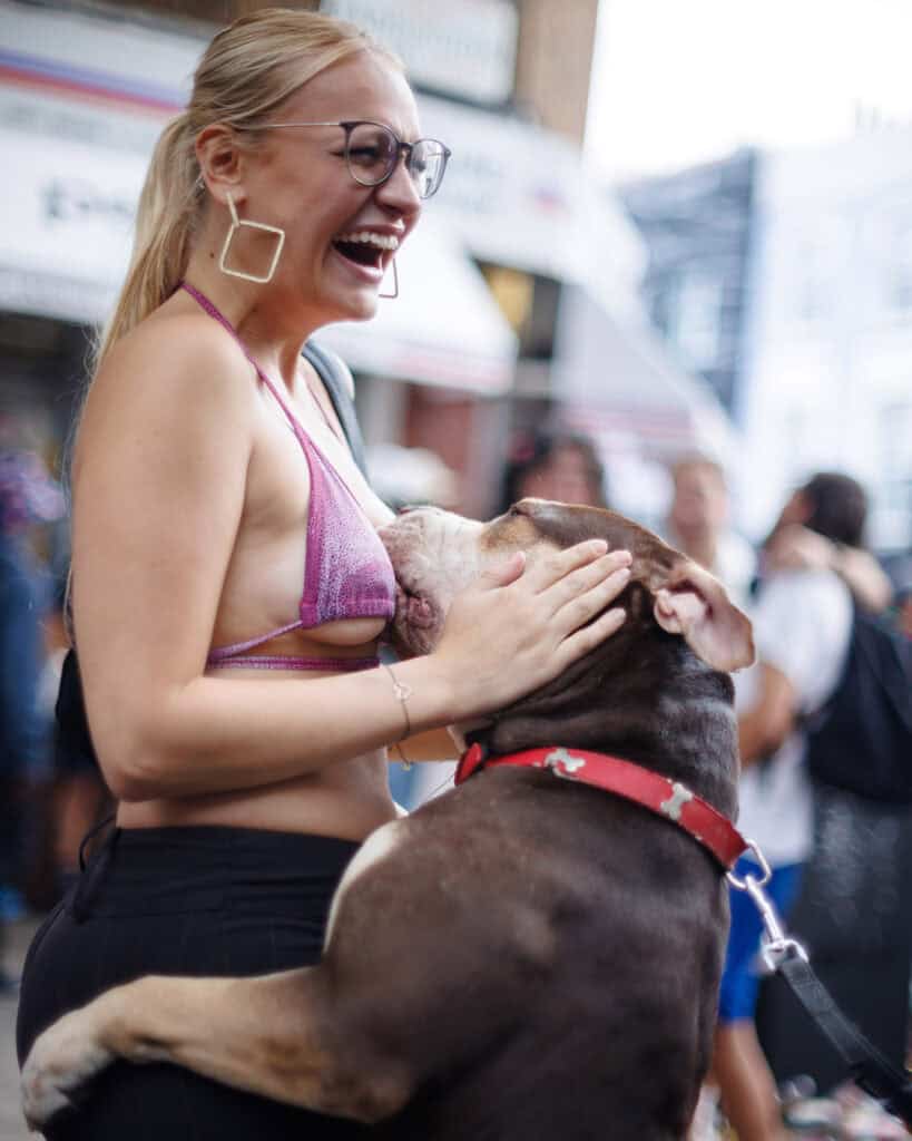 Woman laughing as her dog jumps up during Notting Hill Carnival.