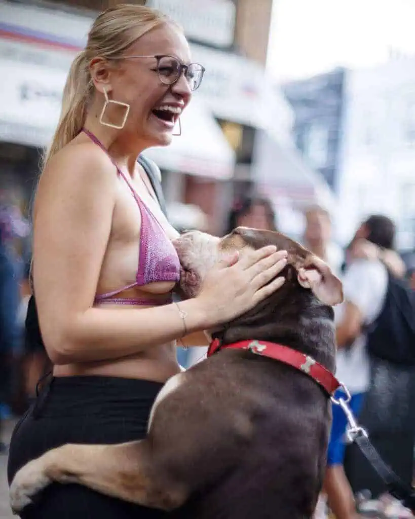 Woman laughing as her dog jumps up during Notting Hill Carnival.