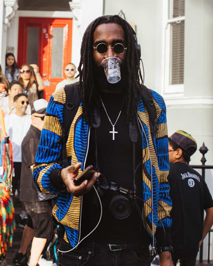 Man in vibrant patterned jacket with a camera enjoying Notting Hill Carnival.