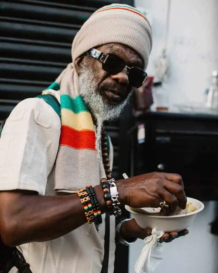 Elder wearing Rastafarian colours eating street food at Notting Hill Carnival.