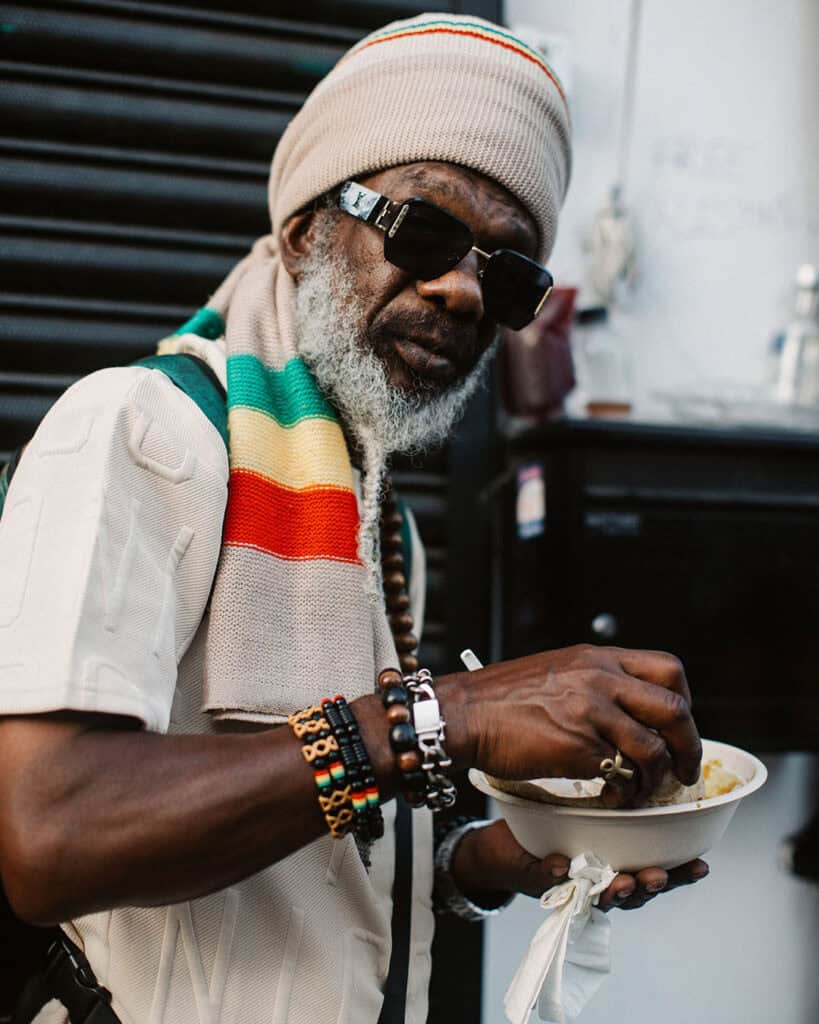 Elder wearing Rastafarian colours eating street food at Notting Hill Carnival.