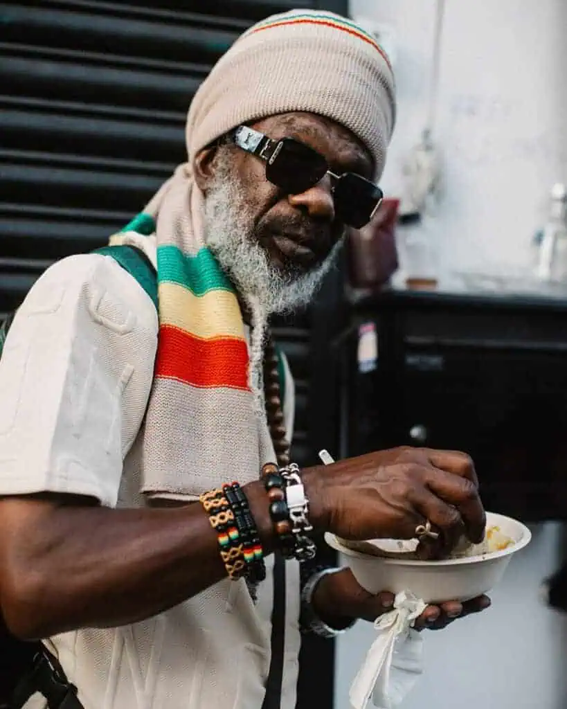 Elder wearing Rastafarian colours eating street food at Notting Hill Carnival.