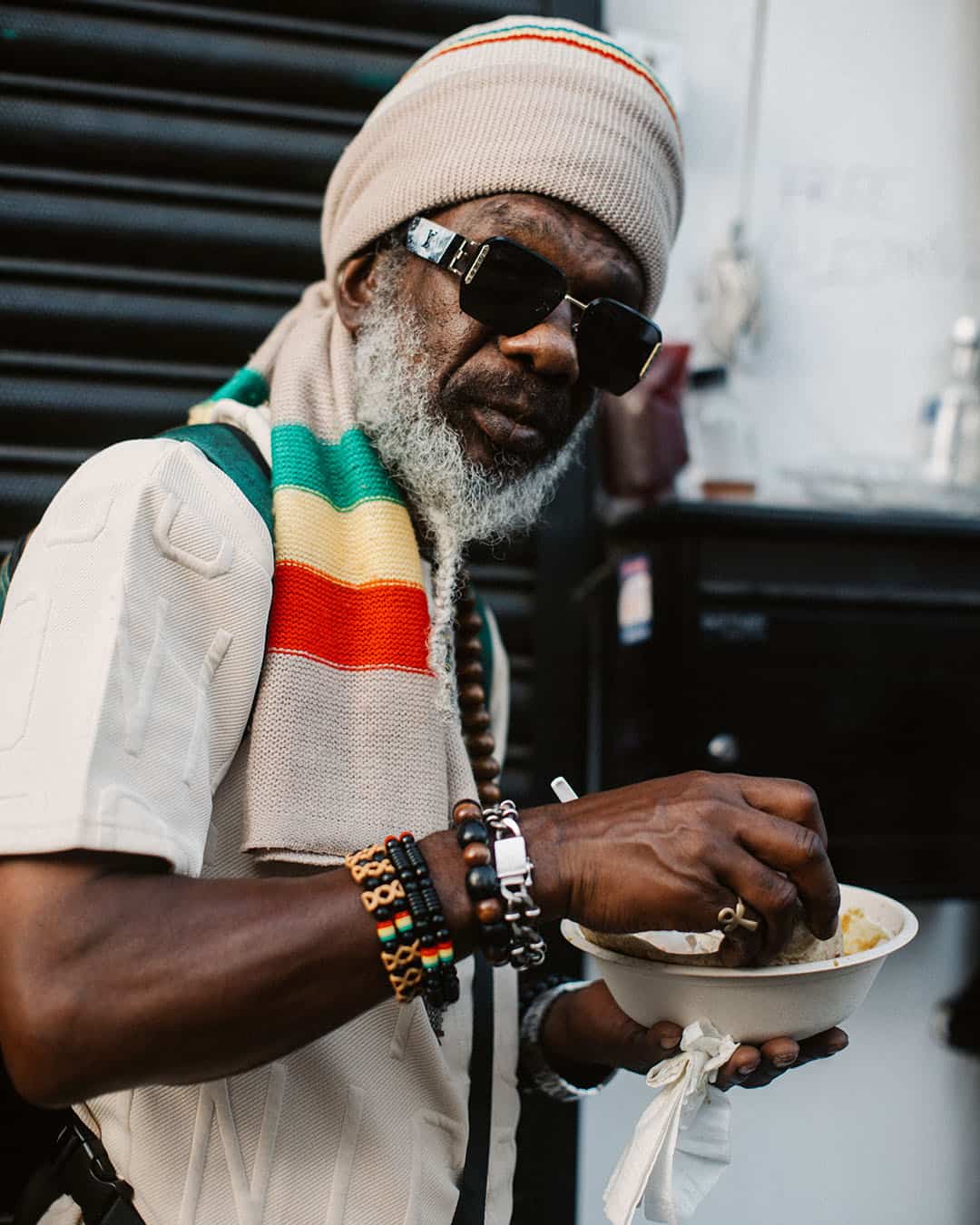 Elder wearing Rastafarian colours eating street food at Notting Hill Carnival.