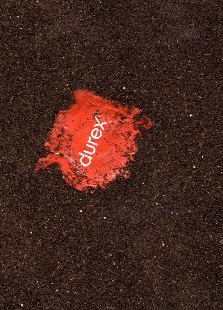 Close-up of a used red condom with the Durex logo on soil, photographed for Cold Magazine’s feature on Cruising Archaeology and queer material culture.