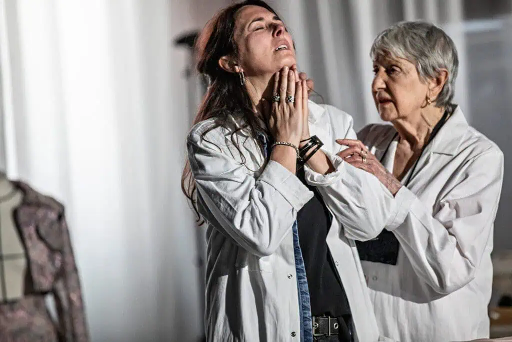 Emotional close-up of two performers in white coats, one looking upward with clasped hands, from Caroline Guiela Nguyen’s LACRIMA, photographed by Jean-Louis Fernandez for Cold Magazine.