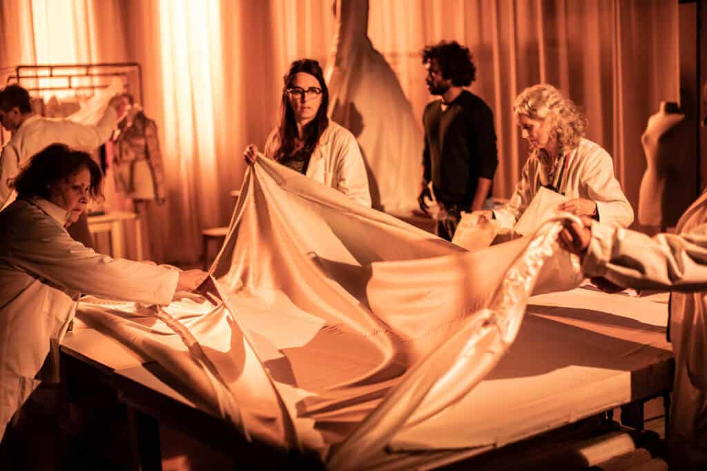 Actors perform a scene from LACRIMA surrounded by flowing white fabric under warm stage lighting, photograph by Jean-Louis Fernandez for Cold Magazine feature on Caroline Guiela Nguyen’s production at the Barbican.