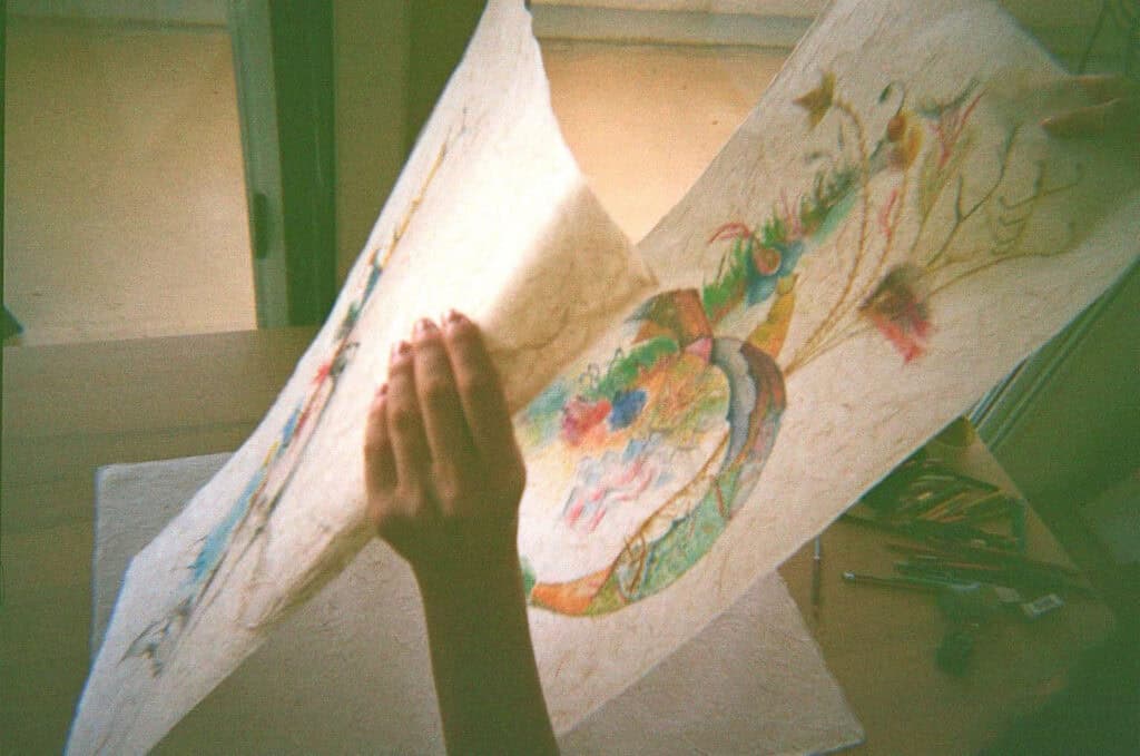 Artist’s hands unfolding a pastel drawing on handmade paper in Valentina Bartolini’s studio, part of her Studio Meditation project.