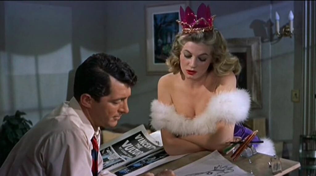 Scene from Artists and Models (1955) showing a man sketching while a woman in glamorous costume leans over, symbolizing art and allure.