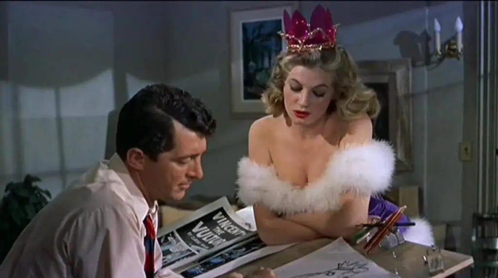 Scene from Artists and Models (1955) showing a man sketching while a woman in glamorous costume leans over, symbolizing art and allure.